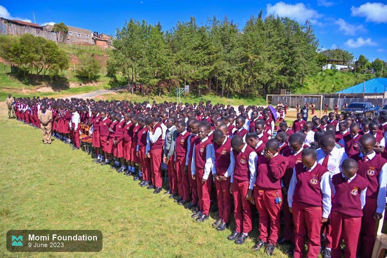 Rows of students in school uniform lined up on a hillside field for the Moi Girls marathon