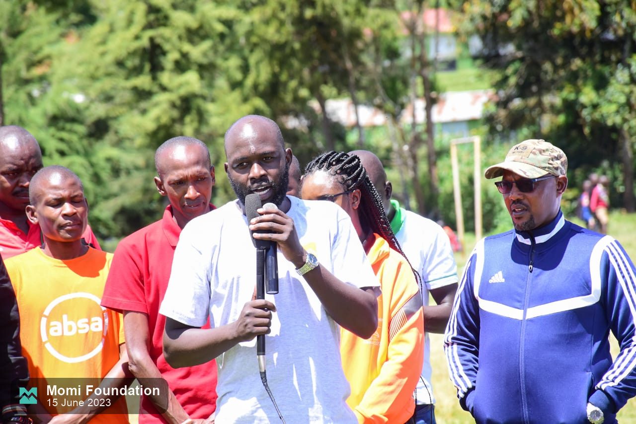 A Momi Foundation speaker addressing runners and supporters with a microphone
