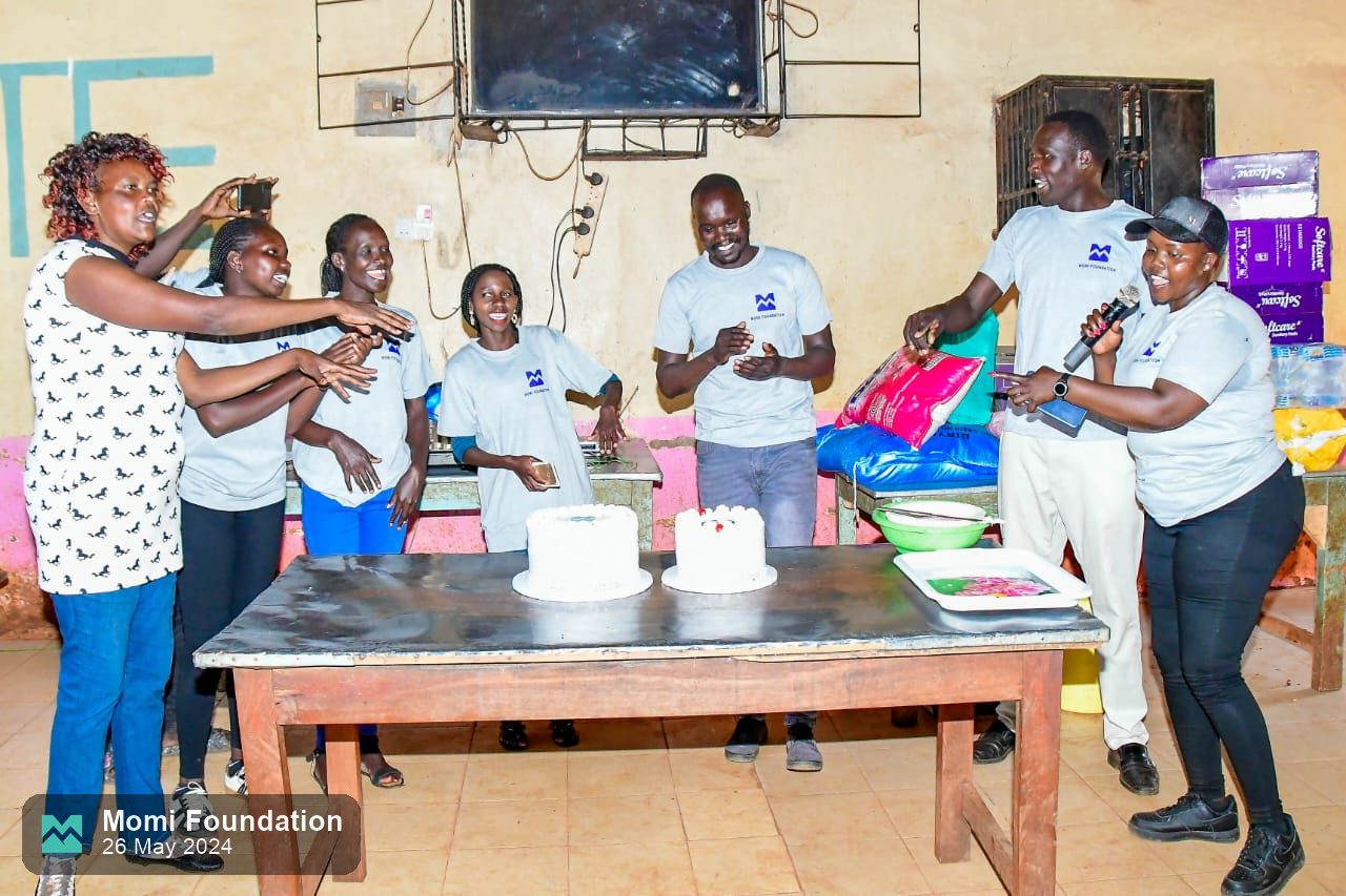 The Momi Foundation team and pupils around a table with cakes in the school hall