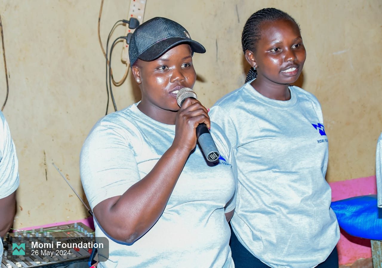 Two Momi Foundation volunteers speaking to the school with a microphone